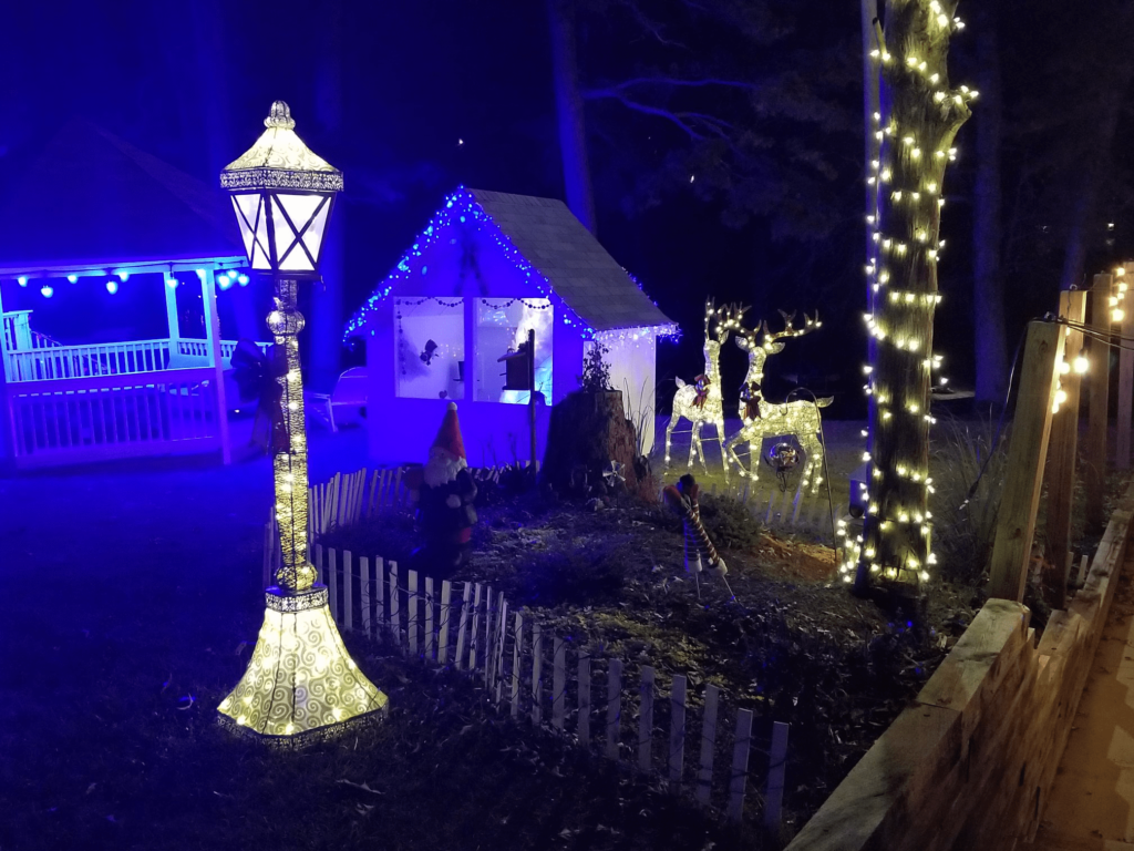 Christmas-themed garden with illuminated lamp post, reindeer lights, and decorative lights on trees and gazebo at night.