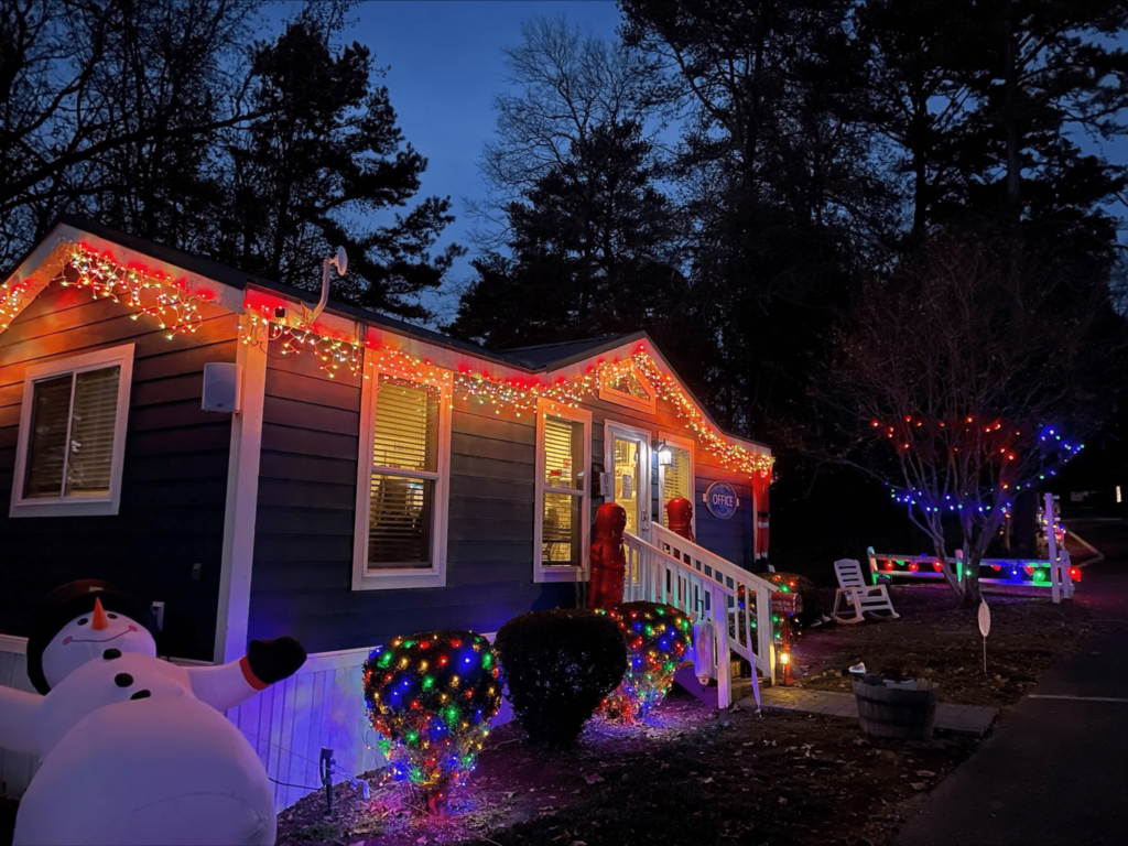 Cabin adorned with colorful Christmas lights at night, featuring a large inflatable snowman and illuminated shrubs.