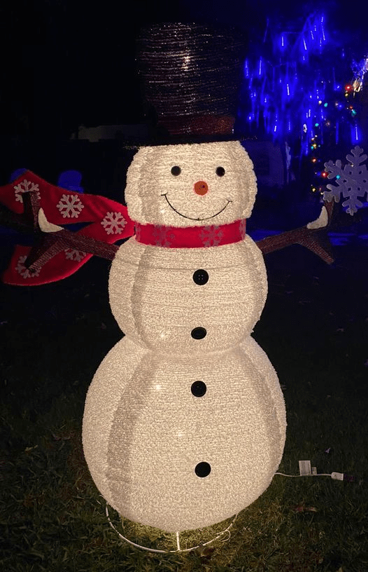 Lighted snowman Christmas decoration with a top hat and red scarf in a nighttime garden setting.